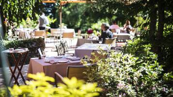 An outdoor dining area with tables and chairs, surrounded by greenery.