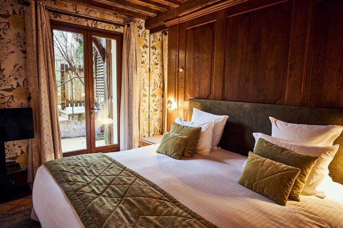 Una habitación de hotel con una cama grande, cabecera de madera y vistas a través de un ventanal.