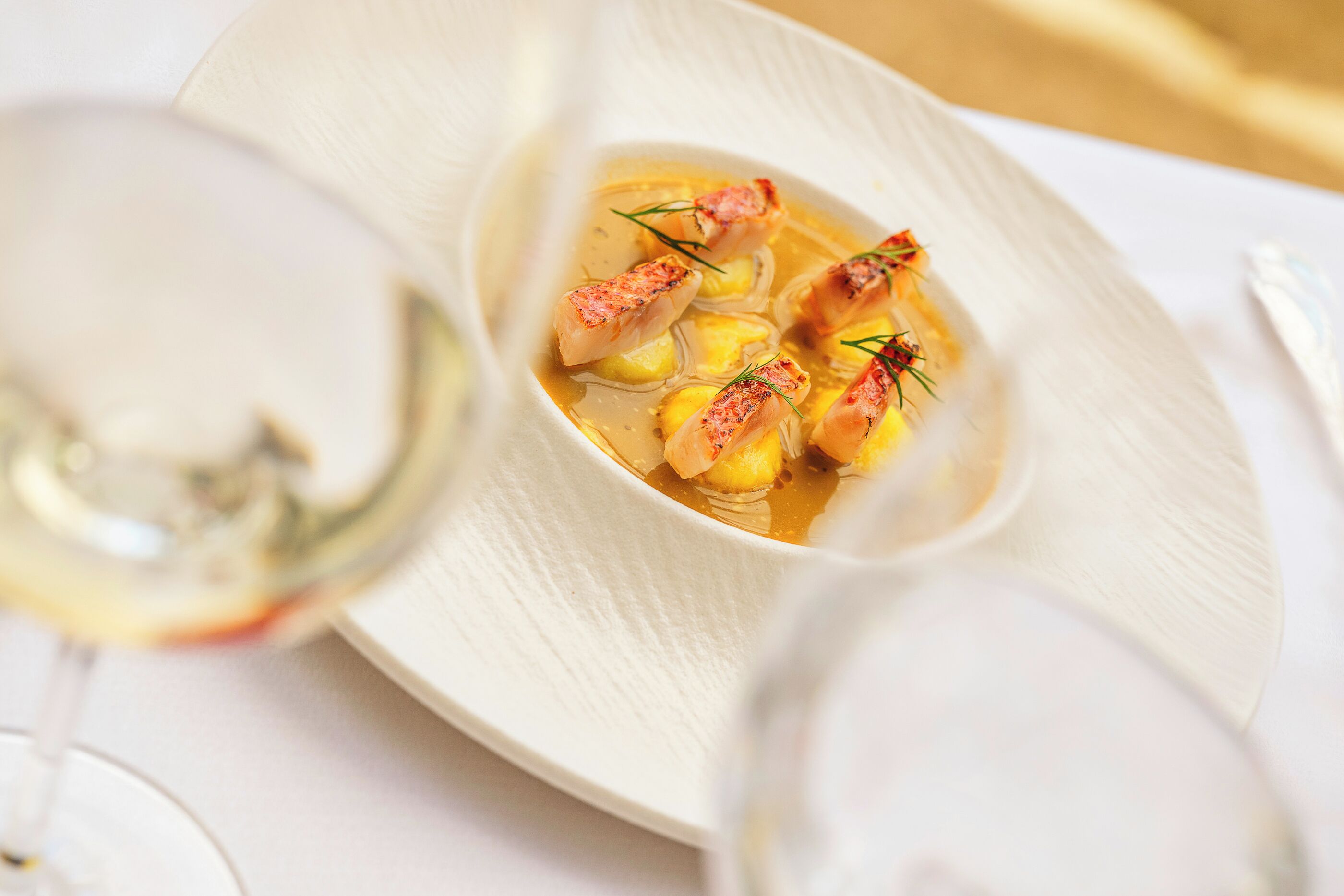 Un plato blanco con un guiso de comida, acompañado de una copa de vino blanco.