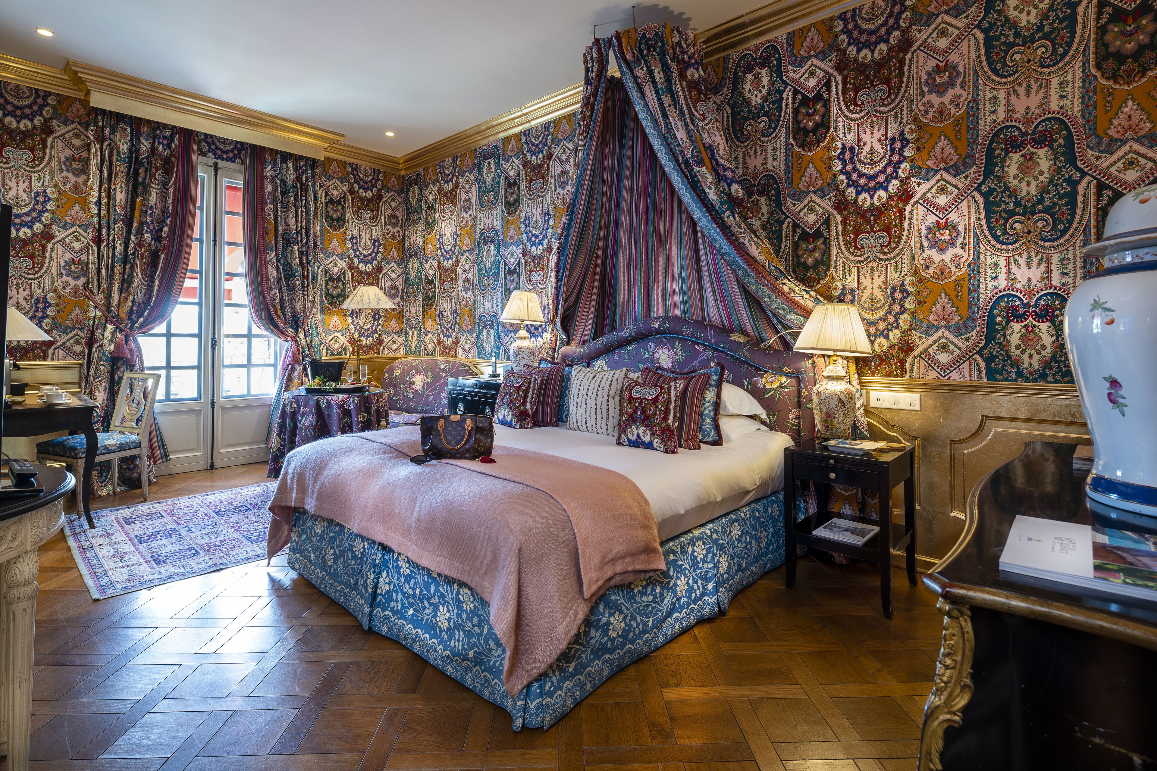 Une chambre spacieuse avec un grand lit, des rideaux décoratifs et un papier peint à motifs.