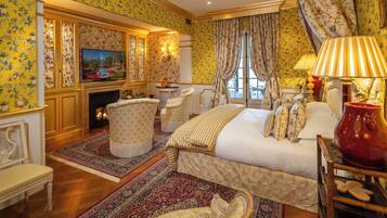 Habitación de hotel con una cama grande, televisión, chimenea y una zona de estar con sillas.
