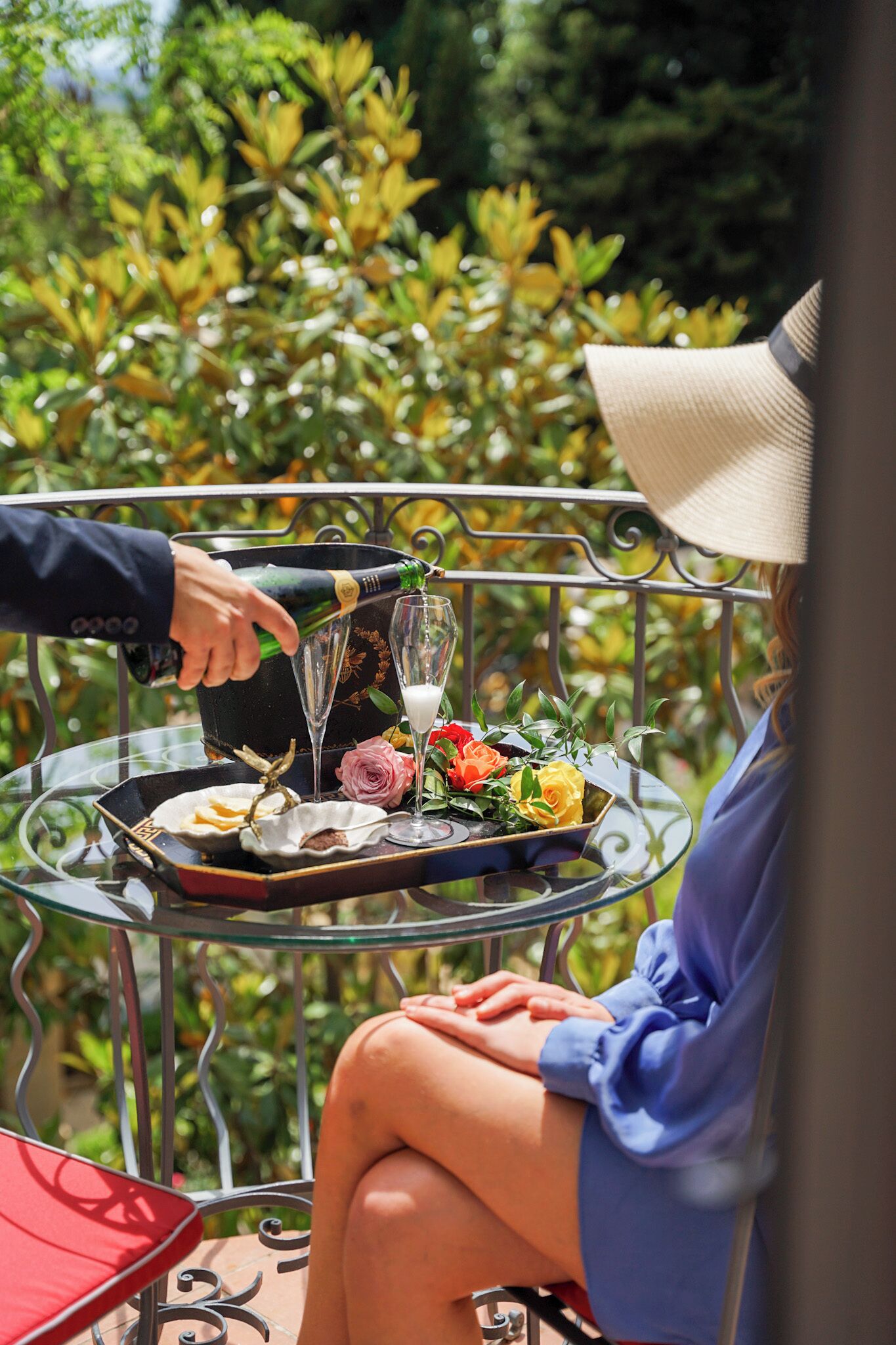 A person pouring champagne into a glass on a table with a tray of food and flowers.