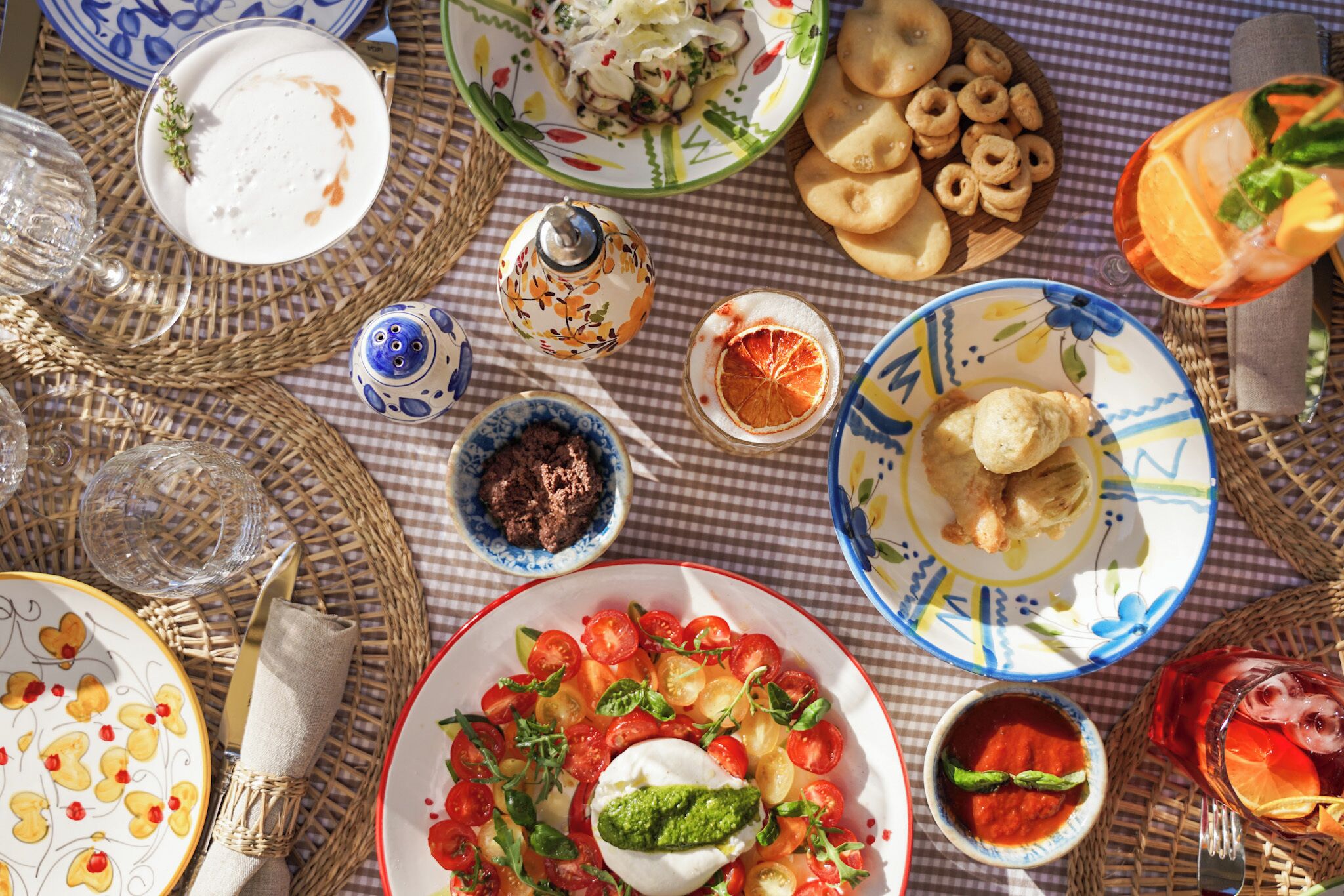 A table set with various dishes, including a salad with tomatoes and a creamy sauce, a bowl of soup, and several glasses of beverages.
