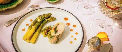 A plate of food with asparagus and a piece of fish, accompanied by a spoon and a fork on a table.
