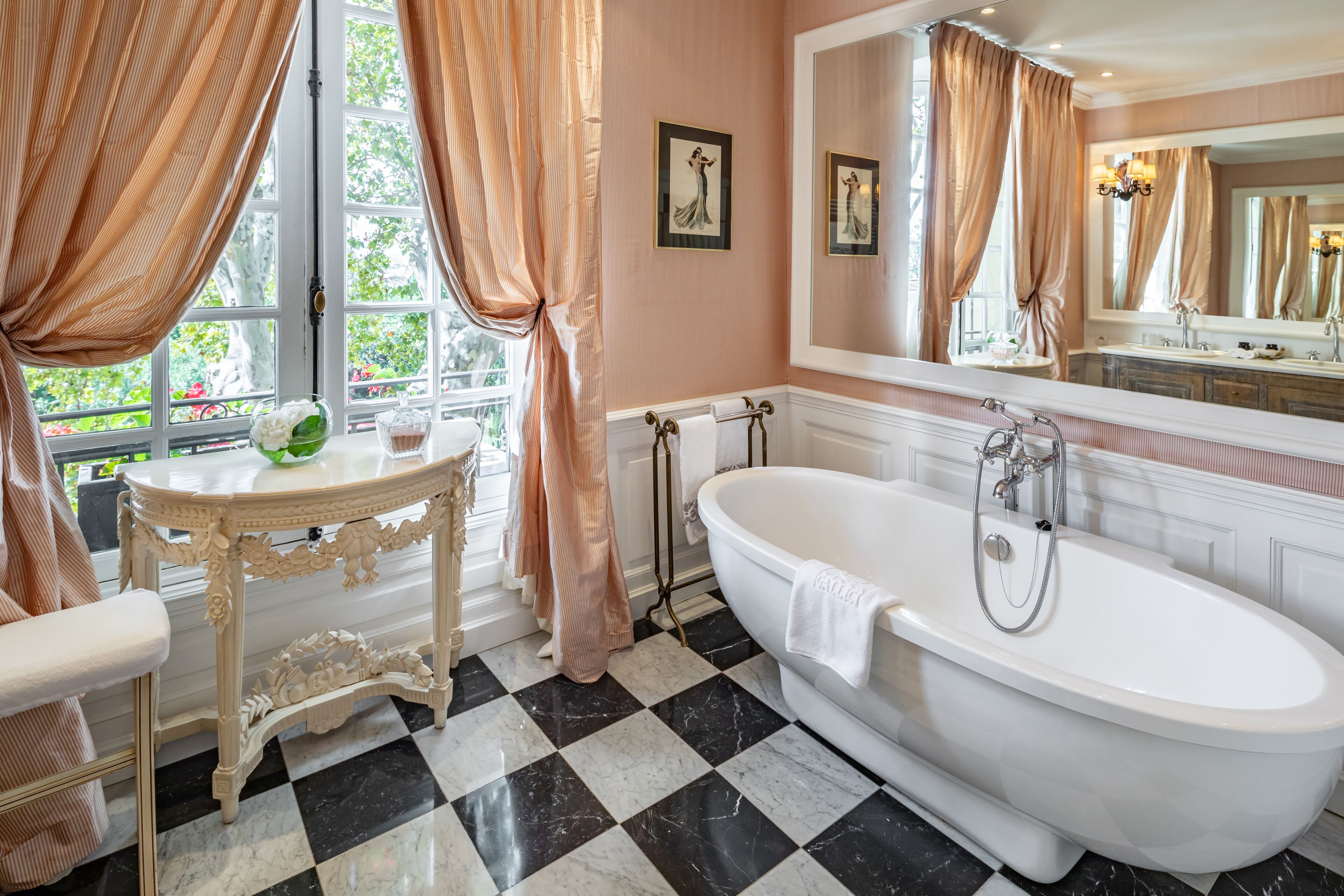 A classic bathroom with a freestanding bathtub, a vanity with a mirror, and a window with curtains.