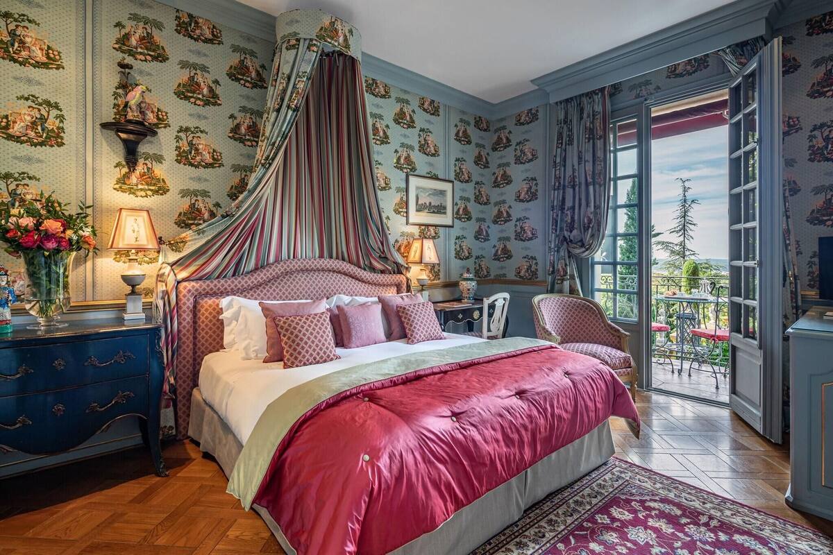 Une chambre à coucher avec un lit à baldaquin, une vue sur l’extérieur, un papier peint à motifs bleus et un plancher en bois.