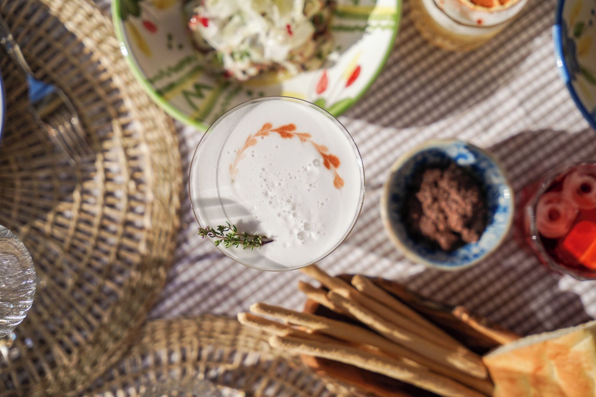 A table with a glass of white beverage, a bowl of chocolate spread, and breadsticks.