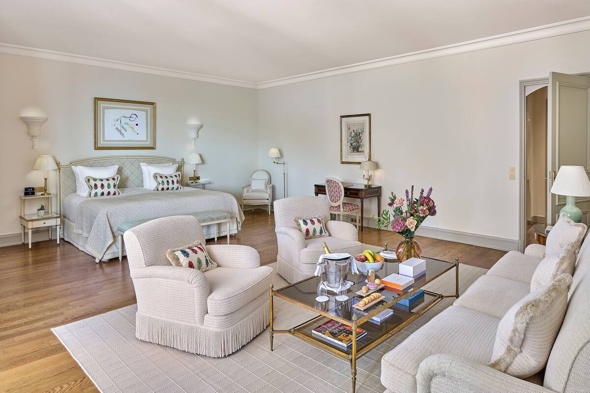 A hotel room with a bed, two armchairs, a coffee table, and a desk with a lamp.