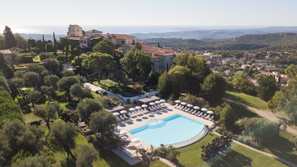 Vue aérienne d’un complexe hôtelier doté d’une piscine, de chaises longues et offrant une vue sur le paysage environnant.