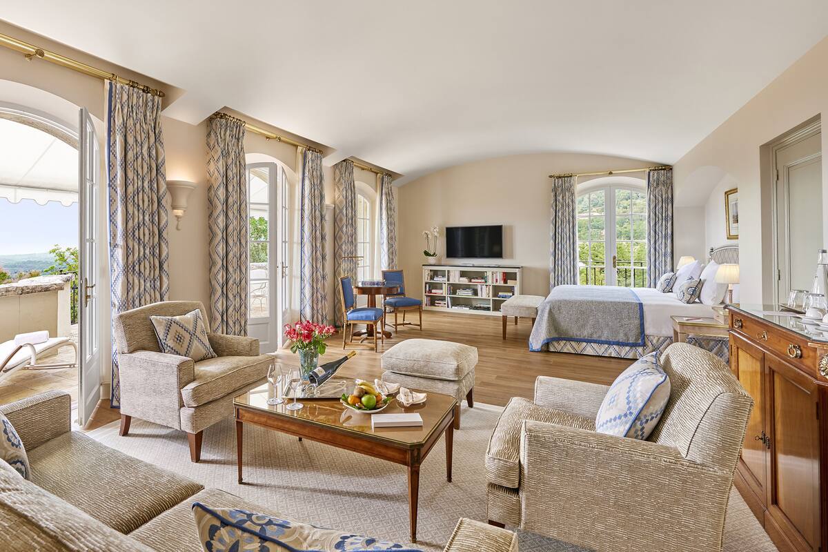 A spacious living room with a large bed, a television, and a balcony with curtains.
