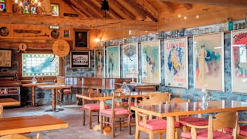 A restaurant interior with wooden tables and chairs, stained glass windows, and various framed artworks on the walls.