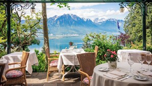 Una terraza con mesas dispuestas para comer, con vistas a un paisaje montañoso y un lago.