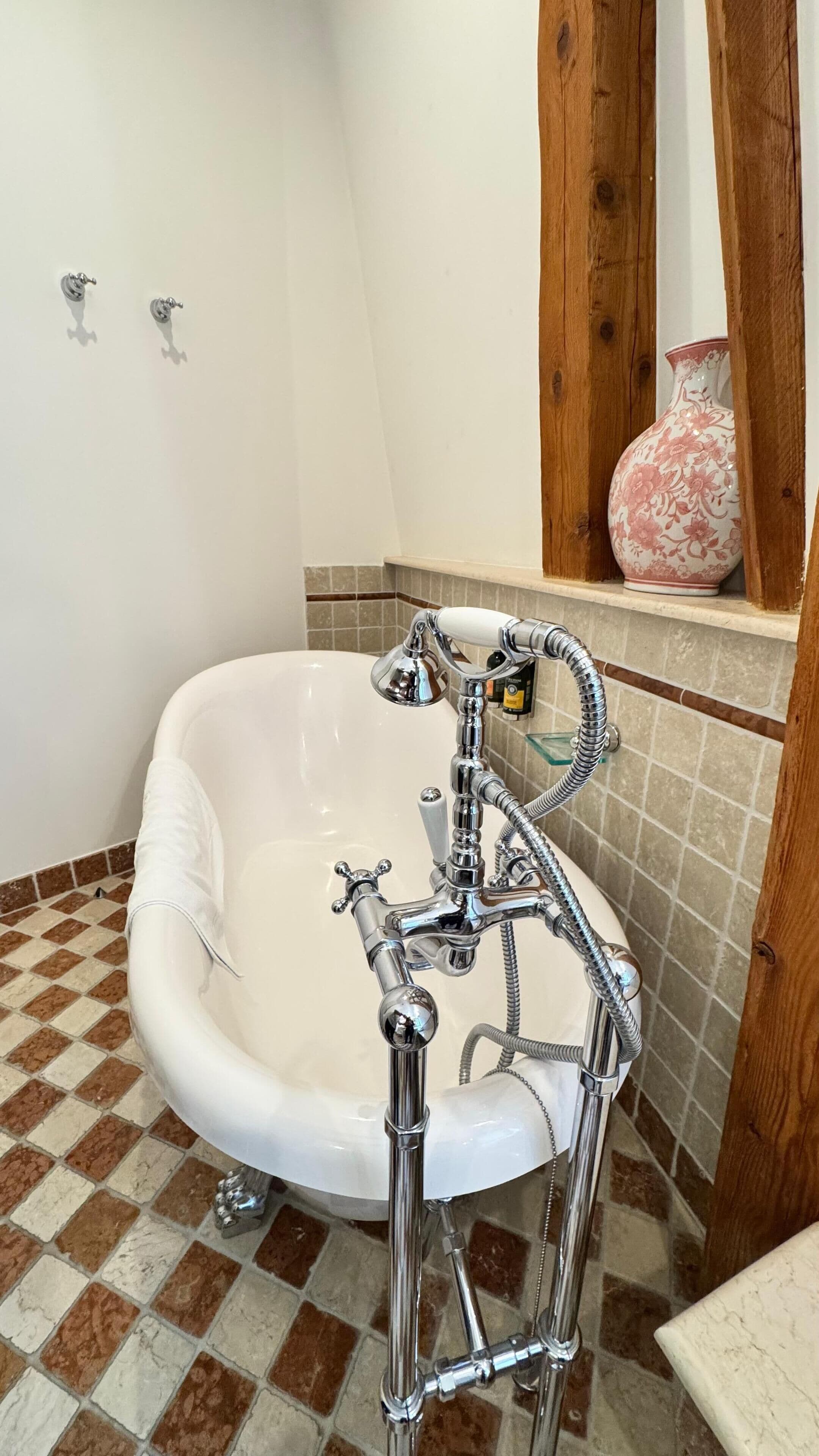 Ein Badezimmer mit einer weißen Badewanne, chromfarbenen Armaturen und einem gefliesten Boden.