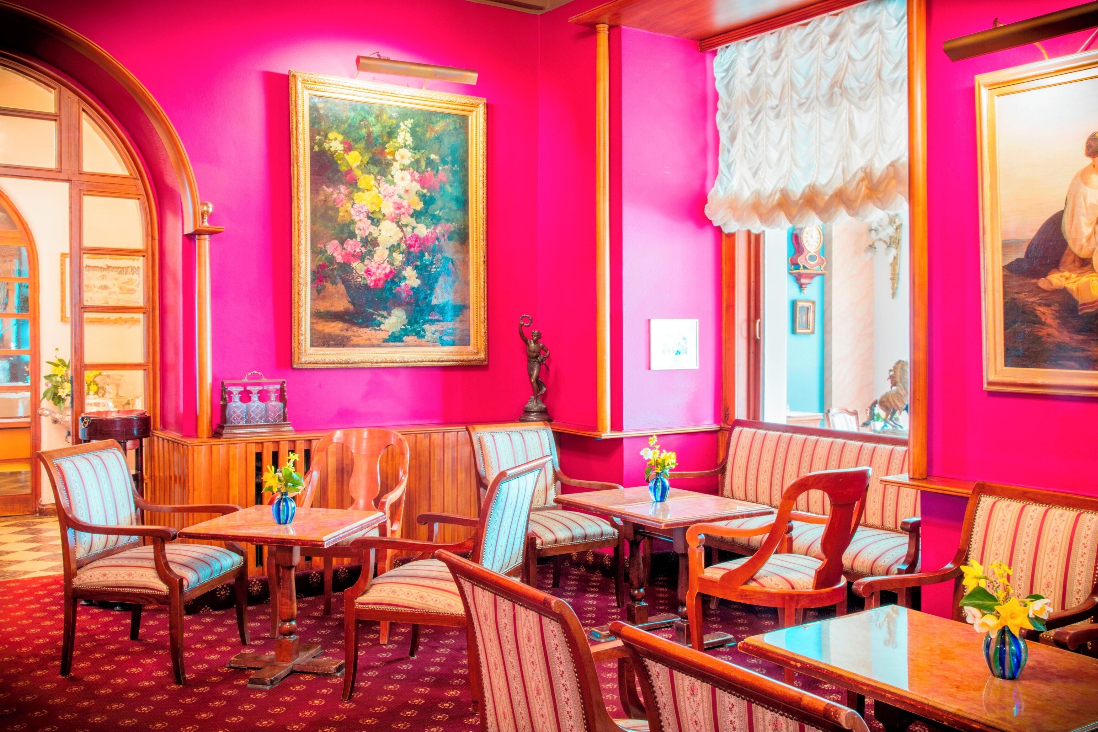 Una habitación con paredes rosa intenso, muebles de madera y obras de arte con motivos florales.