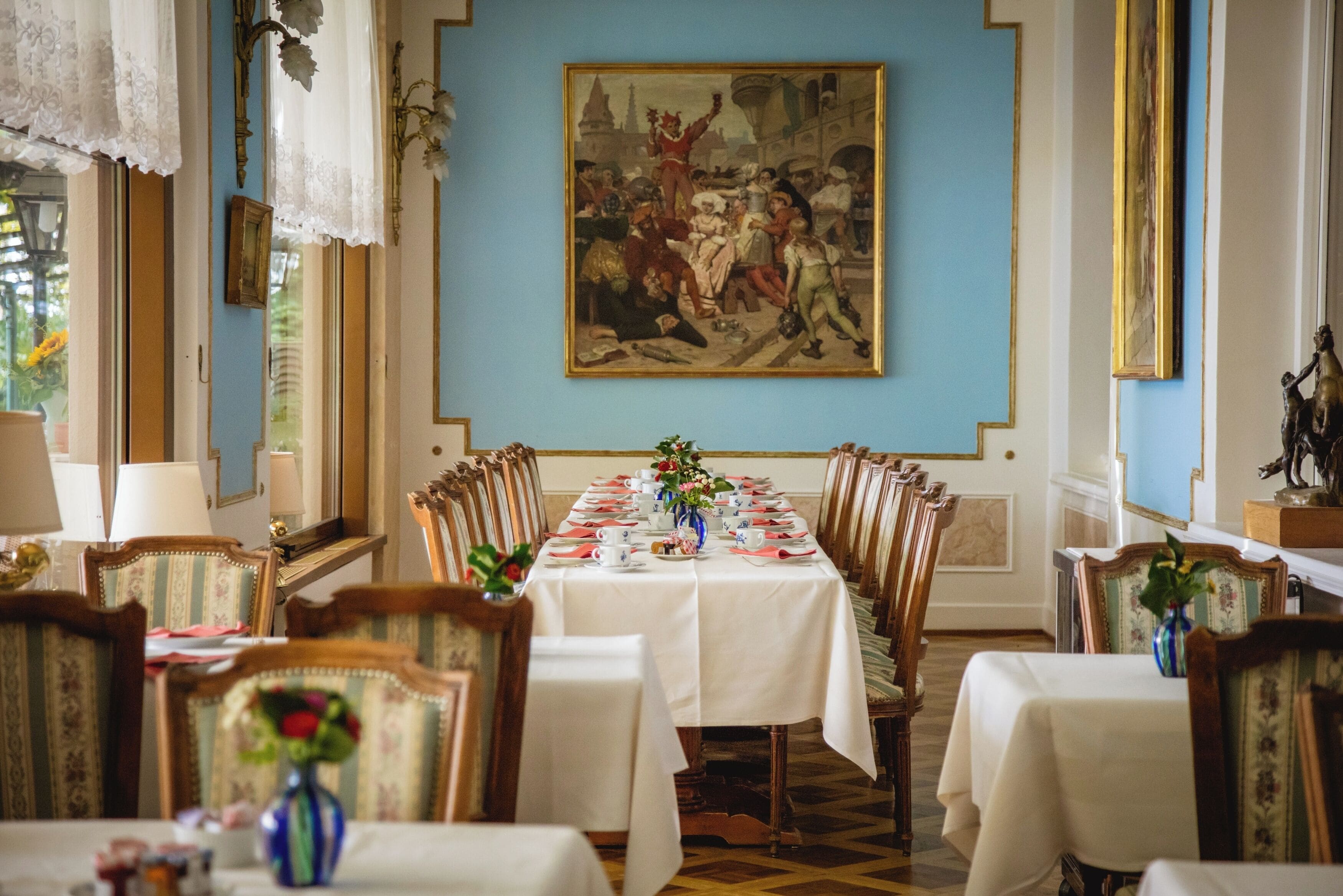 Un comedor con una larga mesa dispuesta para una comida, obras de arte enmarcadas en la pared y sillas de madera clásicas.