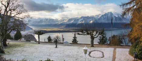 A snowy landscape with a lake, mountains, and a pathway leading to a house.