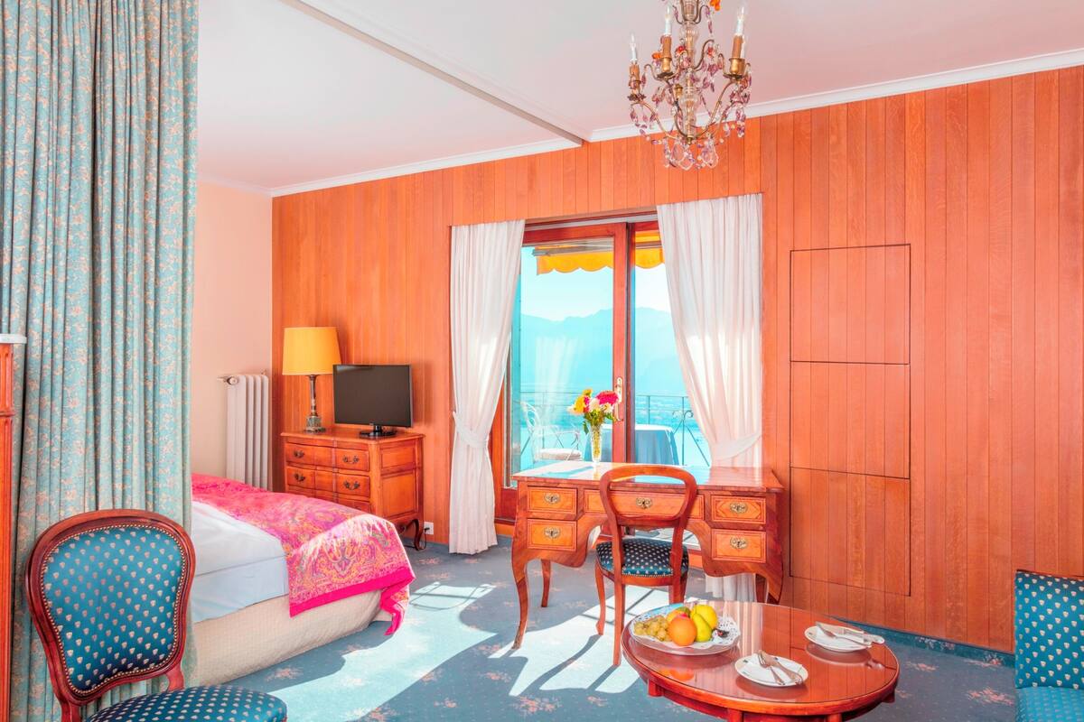 A room with a bed, a desk, a chair, a dining table with fruit, and a TV.