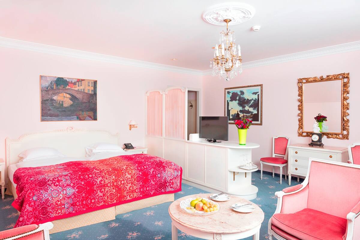 A pink-themed hotel room with a bed, a TV, a desk, a chair, and a mirror.
