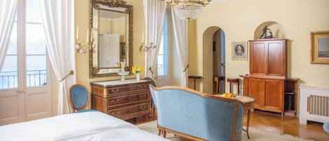 A bedroom with a large bed, a vanity with a mirror, a dresser, a blue armchair, and a chandelier.