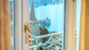A view through a window of a building with a tower and a body of water. - Hotel Victoria (Montreux)
