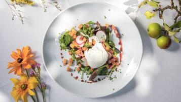Un plato blanco con ensalada, que incluye hojas verdes, rábanos y cubitos de pan tostado, coronado con una cucharada de crema y un chorrito de salsa.