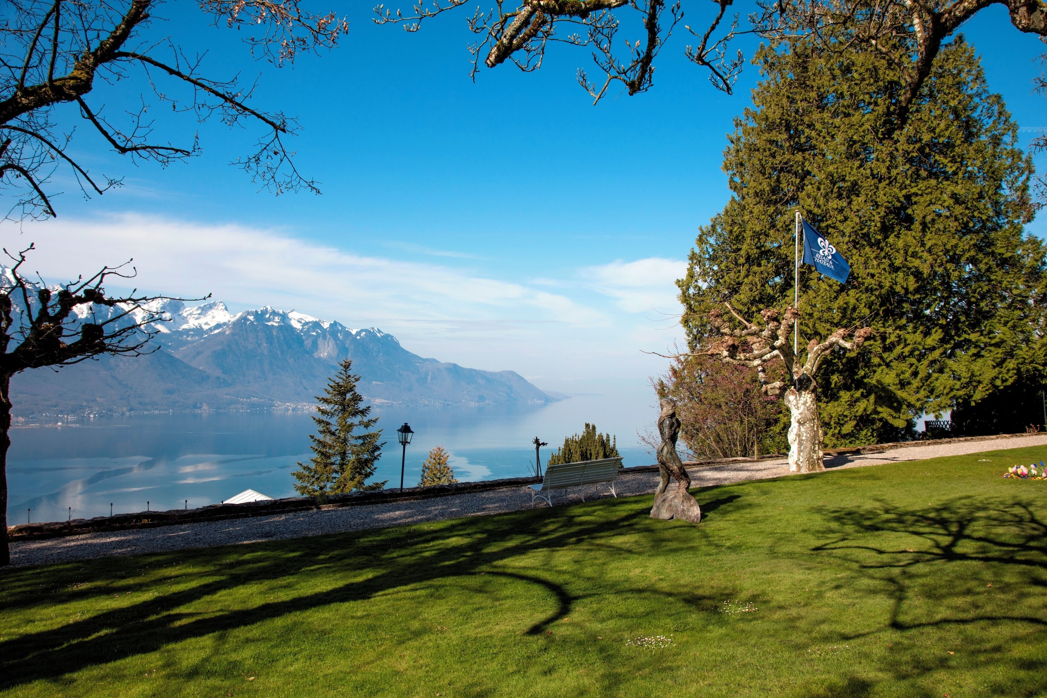 A park with a bench, trees, and a view of mountains and a lake.