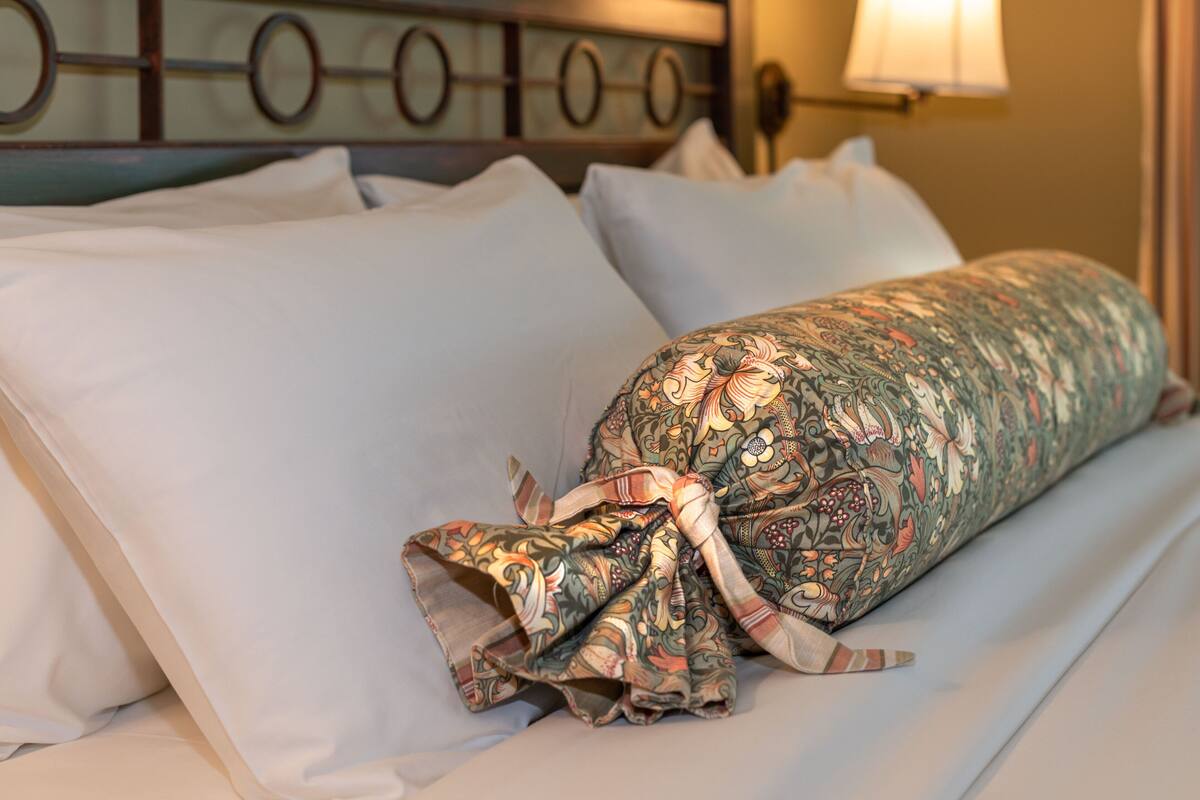 A bed with white pillows and a floral-patterned blanket tied with a striped ribbon.