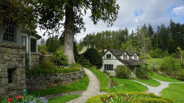A stone house with a garden path leading to a white house surrounded by lush greenery and trees. - Hastings House Country House Hotel (Salt Spring Island)