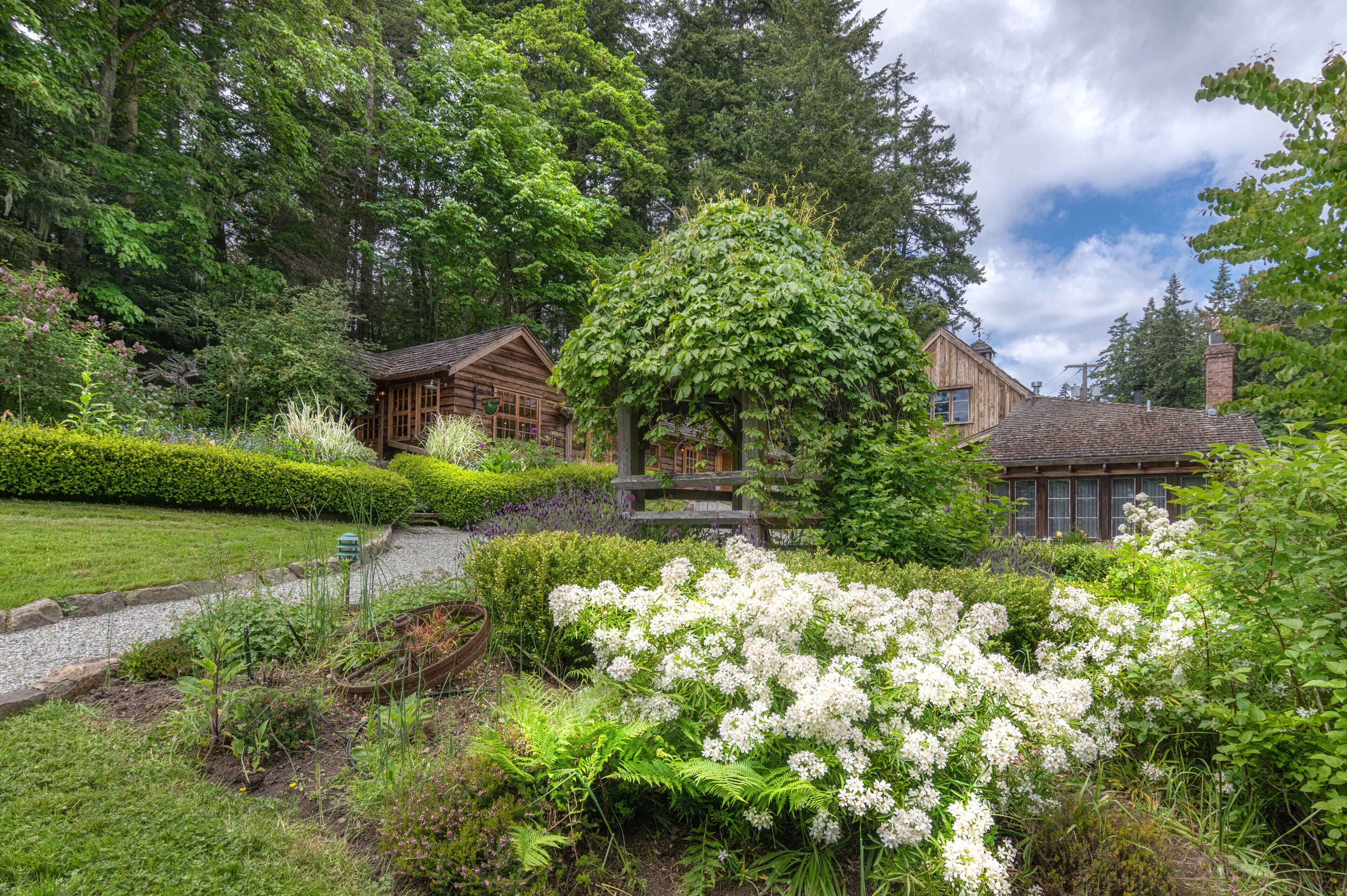 A wooden cabin surrounded by lush greenery and white flowering plants.