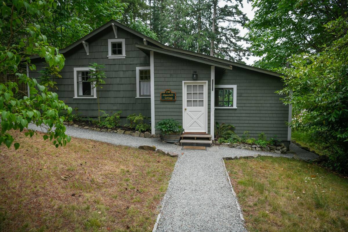 A rustic cabin with a gravel driveway, a white front door, and a small porch area.