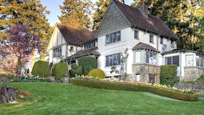 A large, two-story house with a well-maintained lawn and a variety of flowering plants. - Hastings House Country House Hotel (Salt Spring Island)