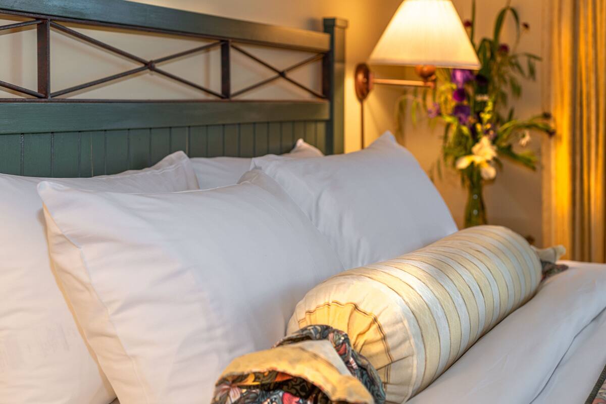 A neatly made bed with white and striped pillows, a wooden headboard, and a wall-mounted lamp.