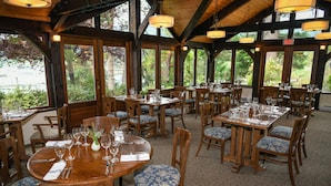 A restaurant with wooden tables and chairs, large windows, and a view of greenery outside. - Hastings House Country House Hotel (Salt Spring Island)