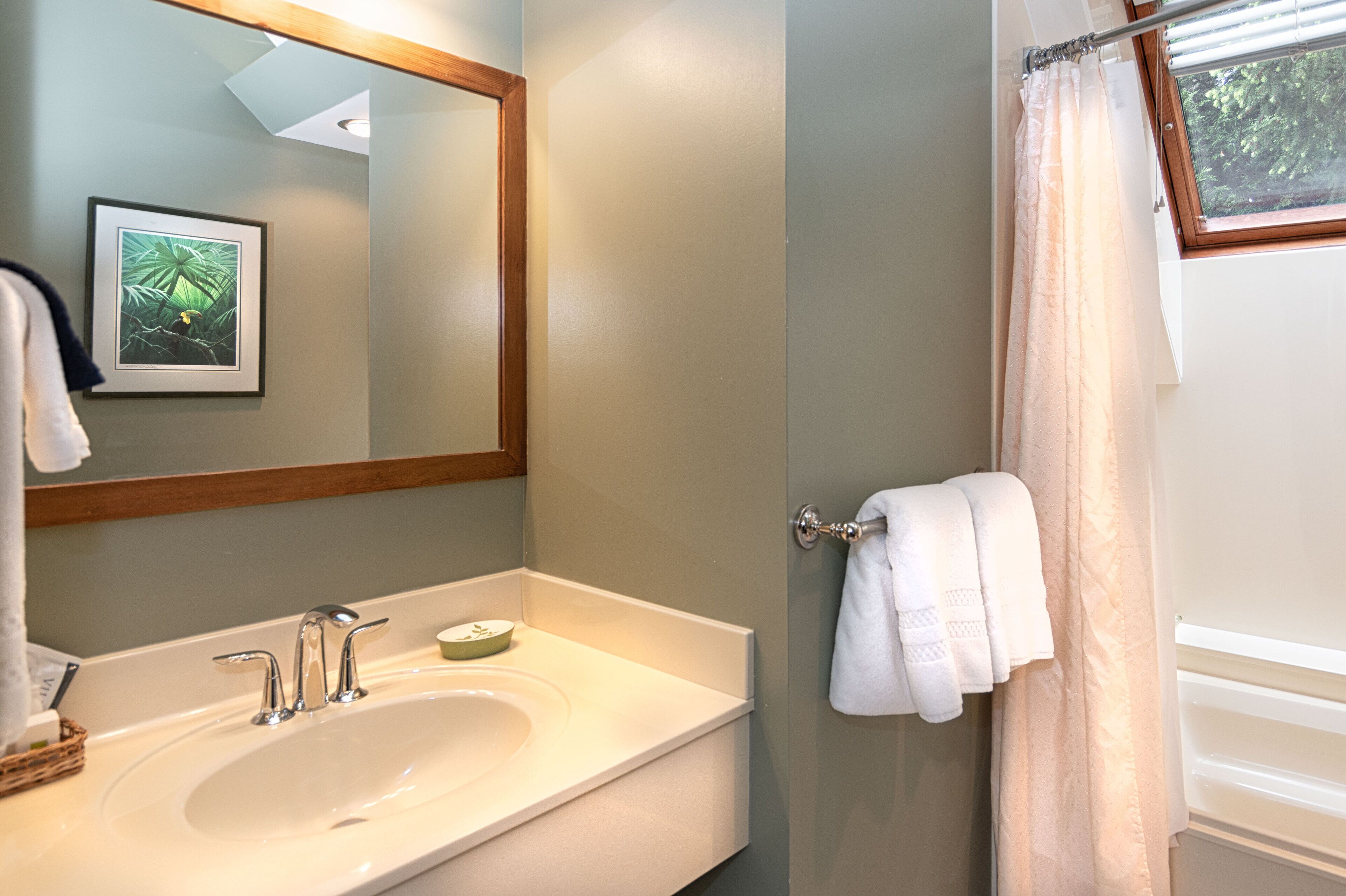 A bathroom with a white sink, a mirror, a framed picture on the wall, and a towel rack with a towel.