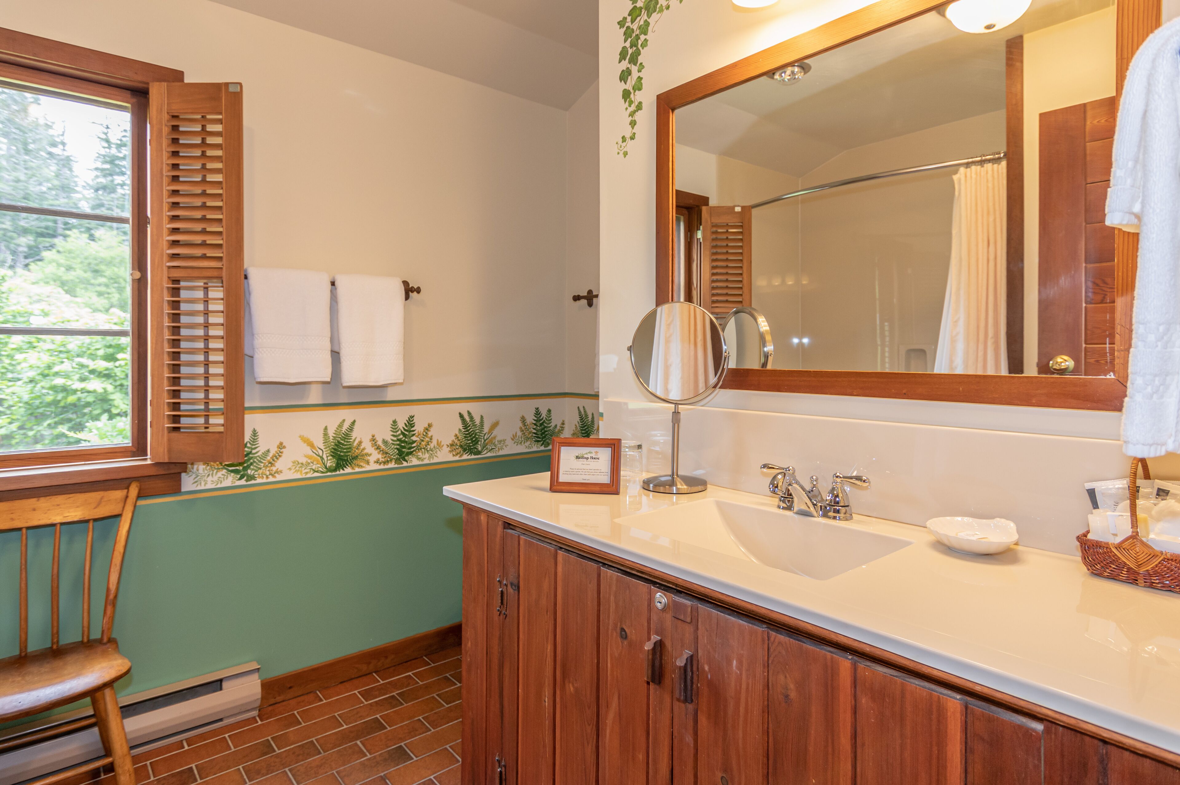 A bathroom with a wooden cabinet, a sink, a mirror, and a window with shutters.