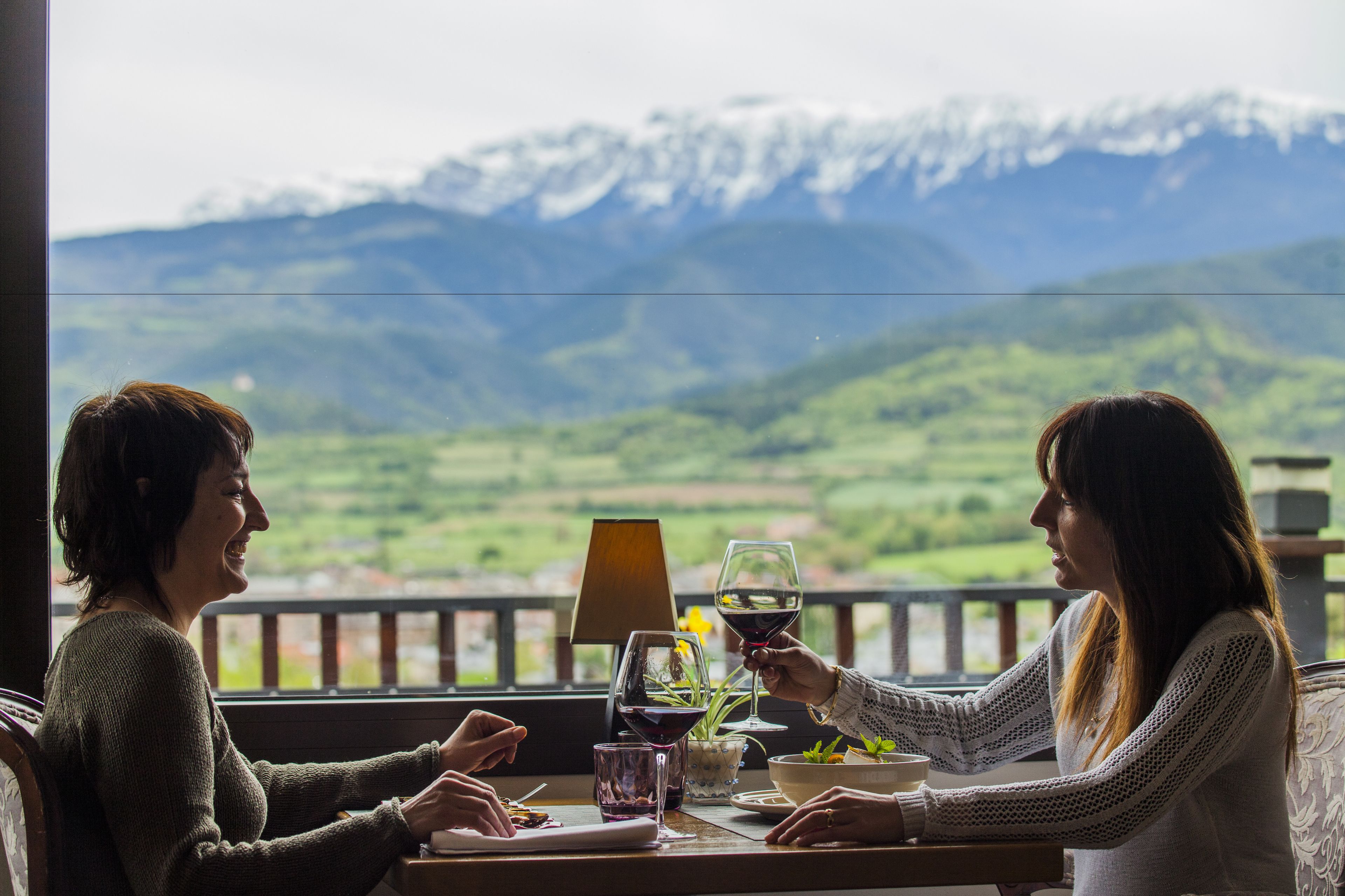 Two people seated at a table with a mountain view, a lamp, and a glass of wine.