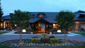 A large, two-story house with a prominent entrance, a landscaped garden with various plants and flowers, and a well-maintained lawn.