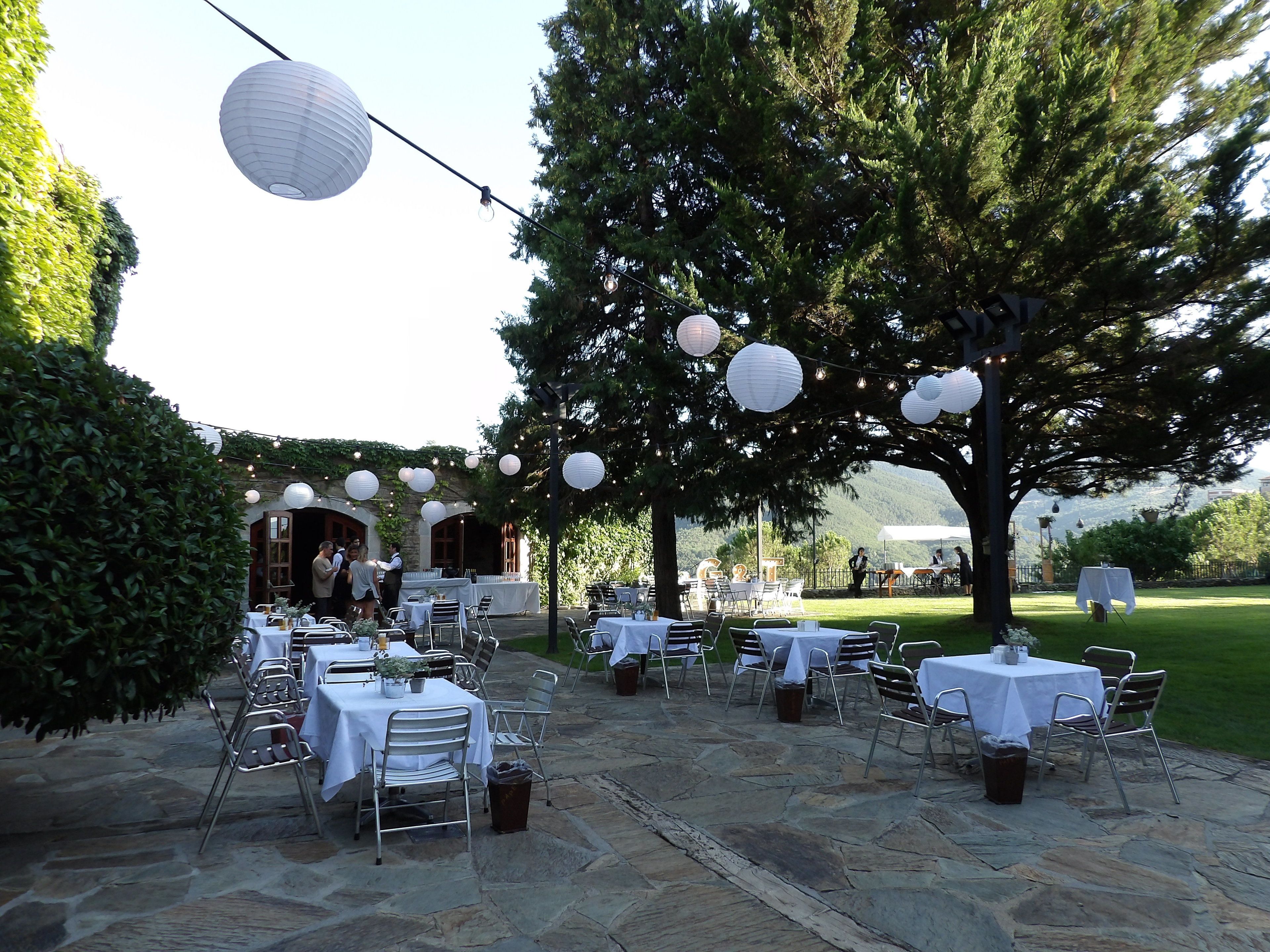 Un área de comedor al aire libre con piso de piedra, manteles blancos y sillas de metal.