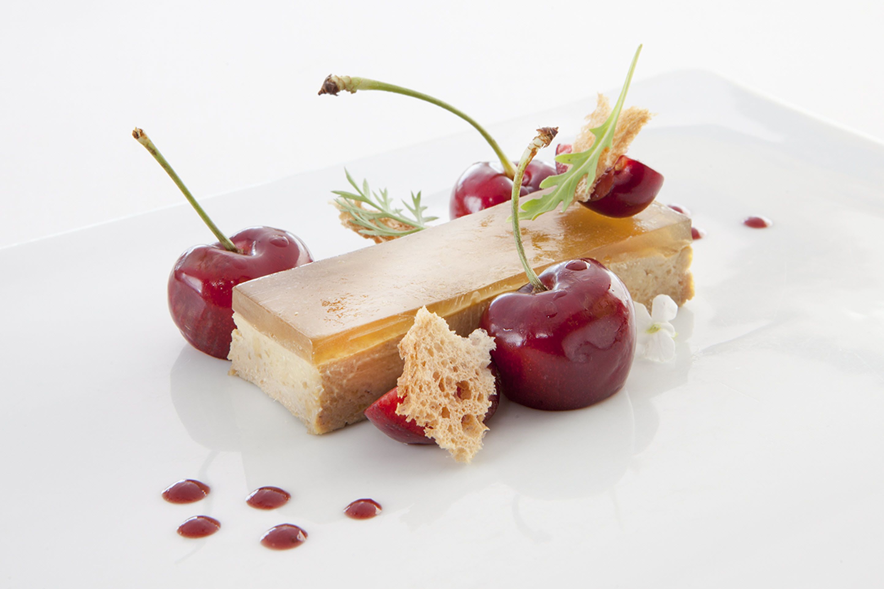 Ein Dessertteller mit einer mehrschichtigen Torte, Kirschen und einem Stück Brot.