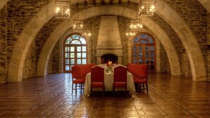 A stone-walled dining area with a fireplace, arched ceilings, and a long table set for a meal.