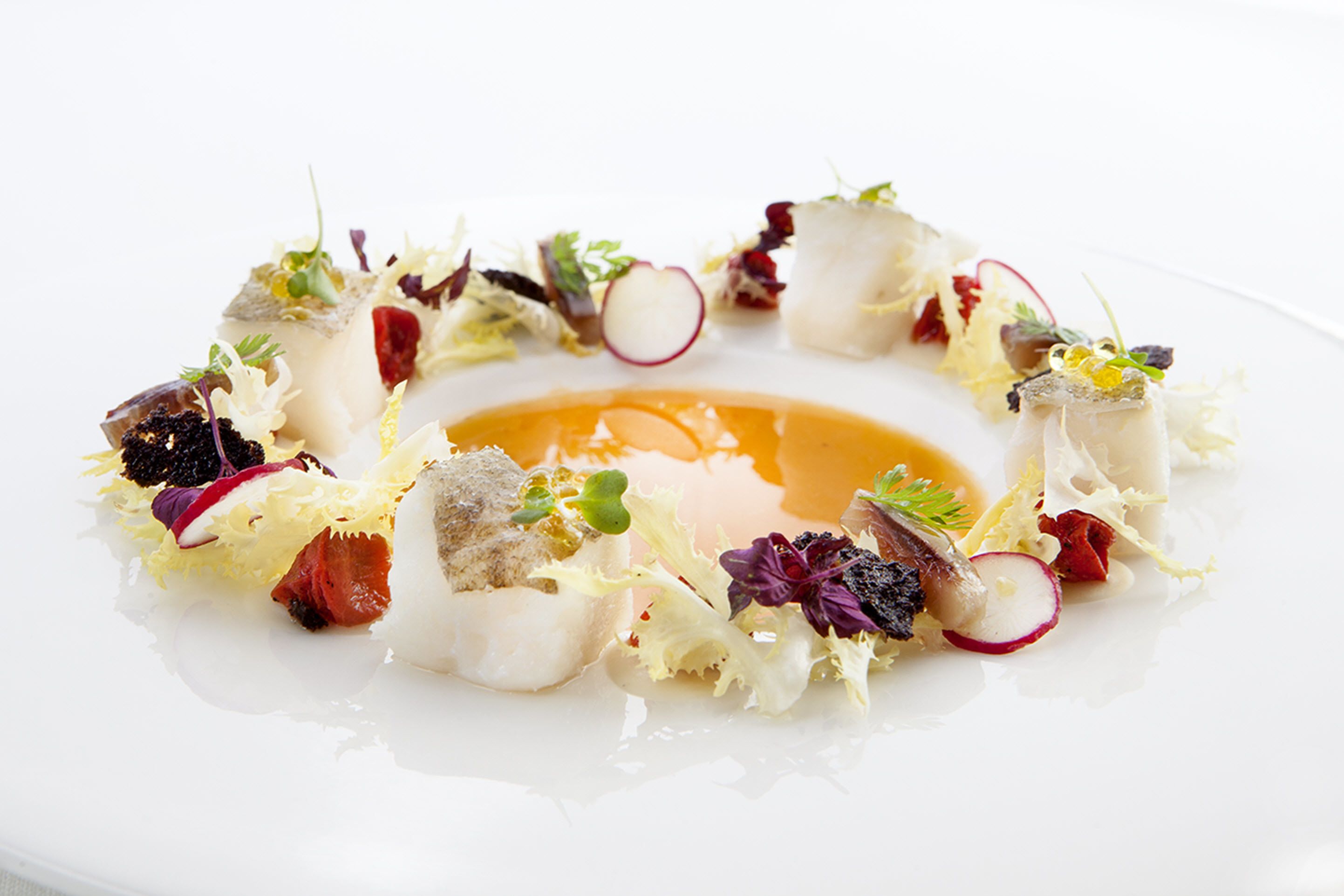A white plate with a variety of food items including fish, vegetables, and a sauce.