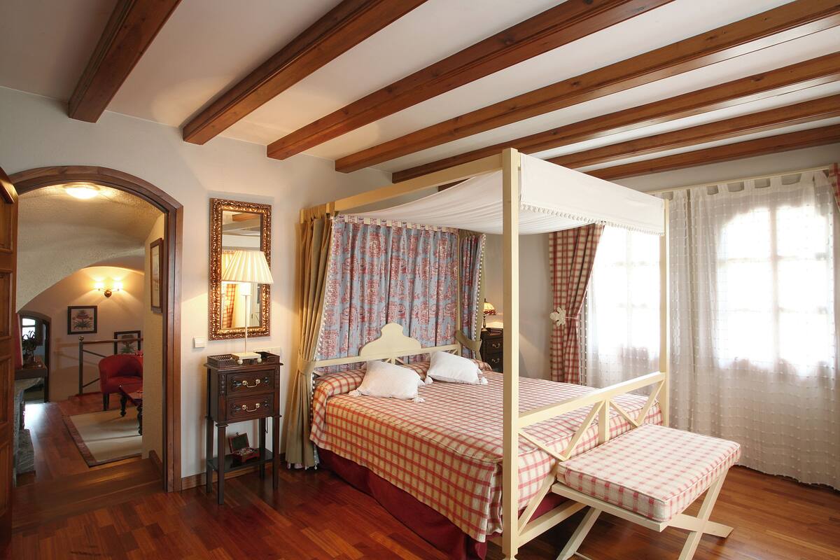 A bedroom with a four-poster bed, a wooden ceiling, and a mirror on the wall.