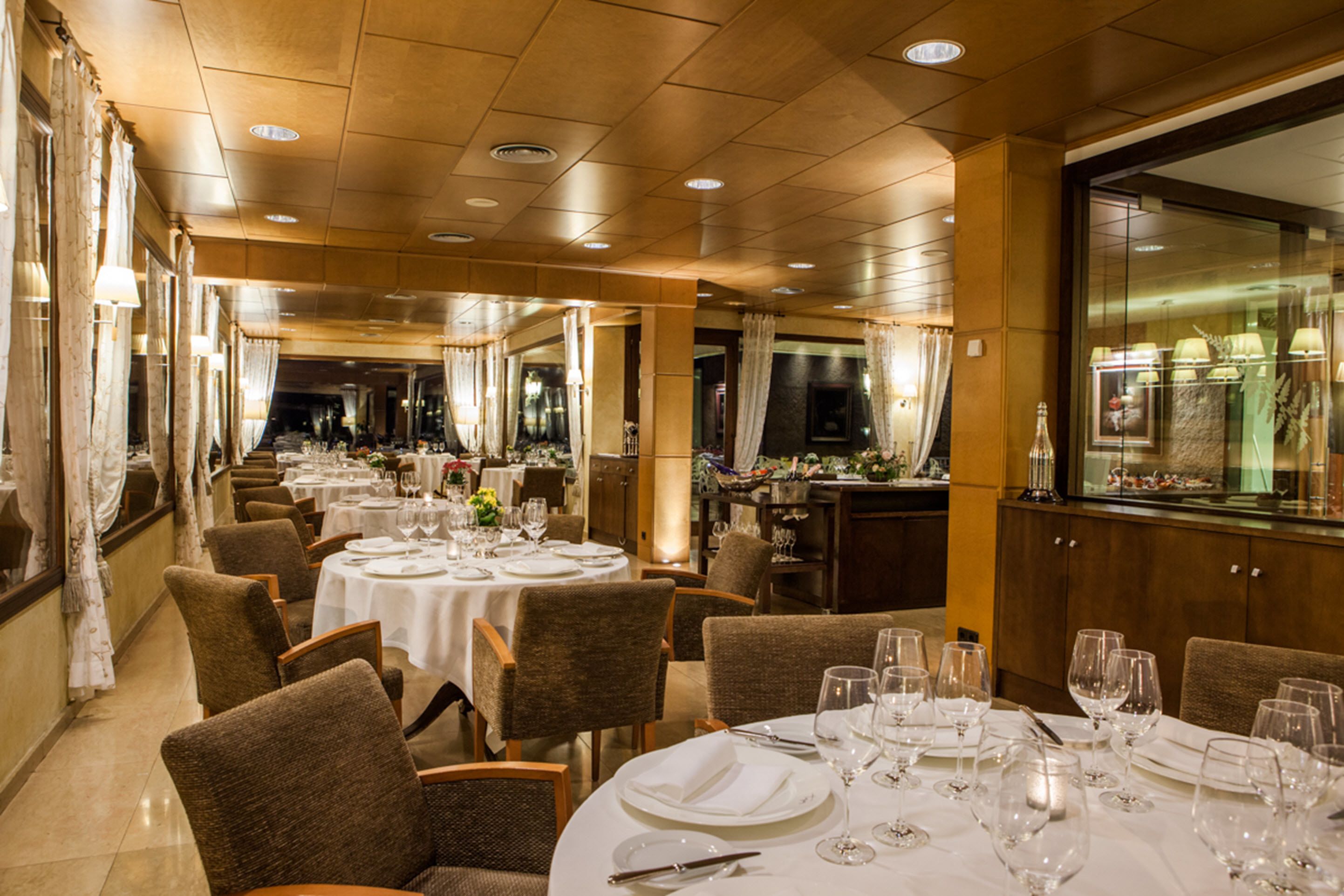 A restaurant with round tables set for dining, featuring white tablecloths and wine glasses.