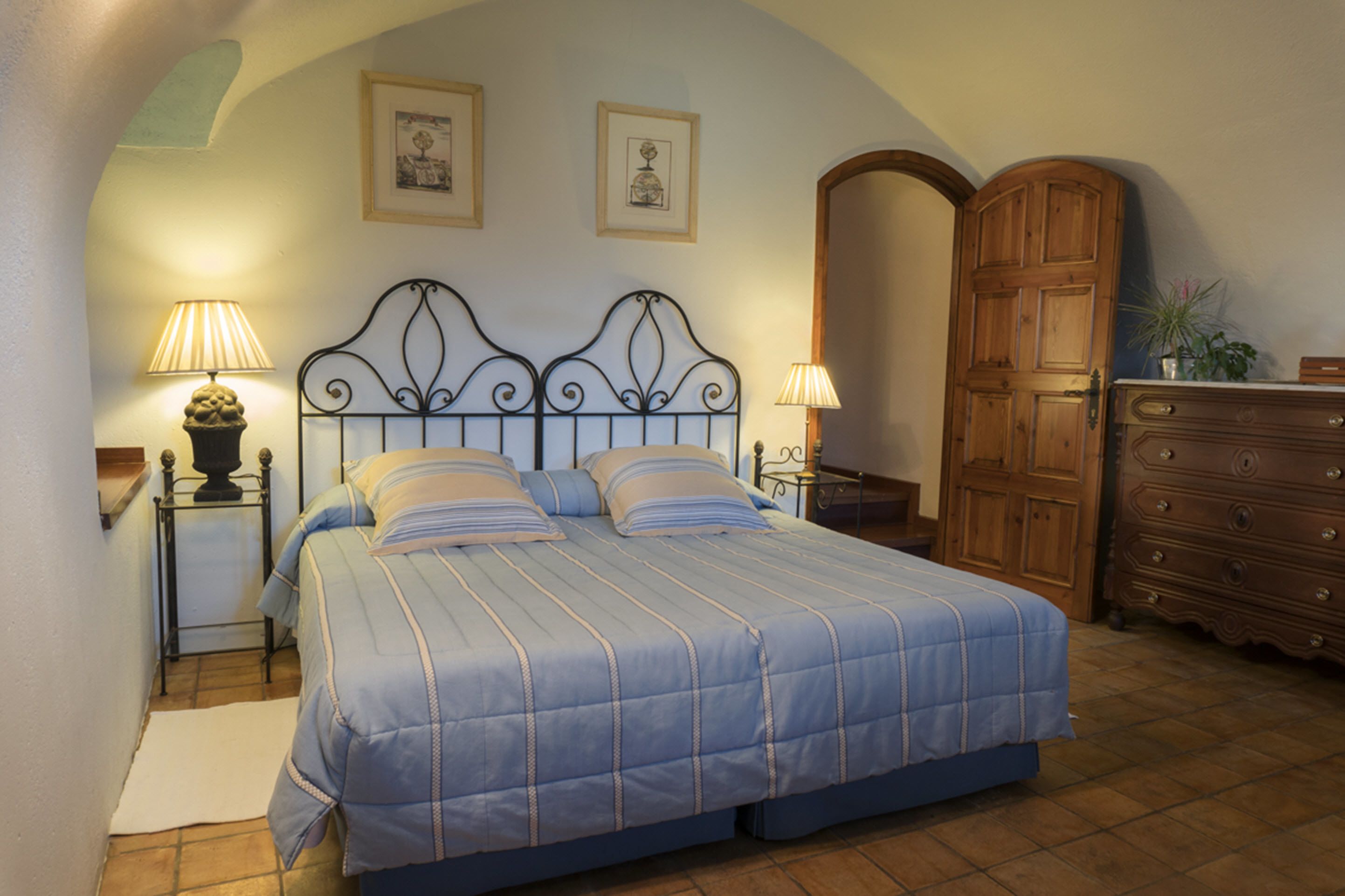 A bedroom with a bed, two bedside tables with lamps, a dresser, and a wooden door.