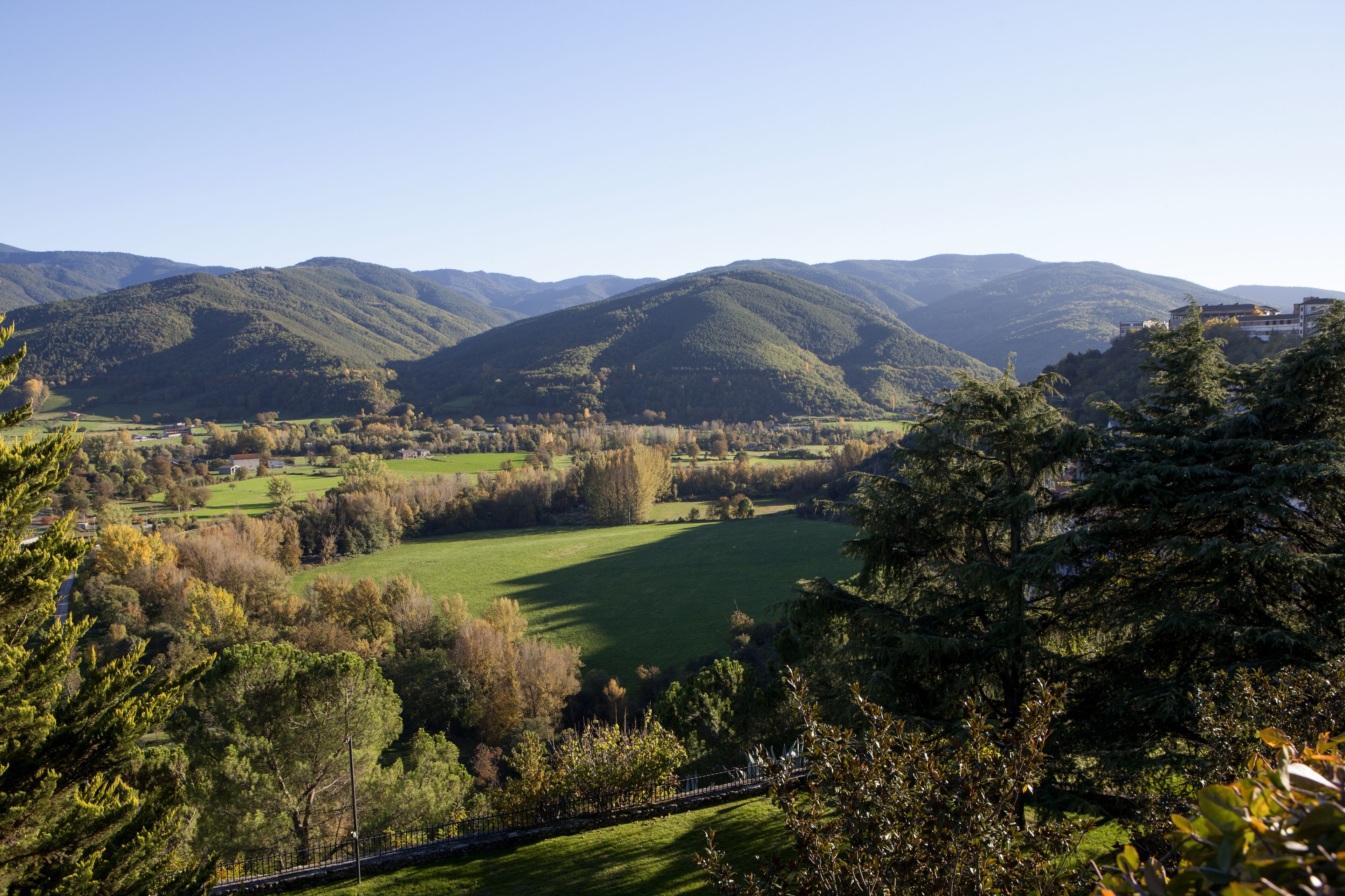 Uma vista panorâmica de um vale com colinas ondulantes, uma ponte e edifícios espalhados.