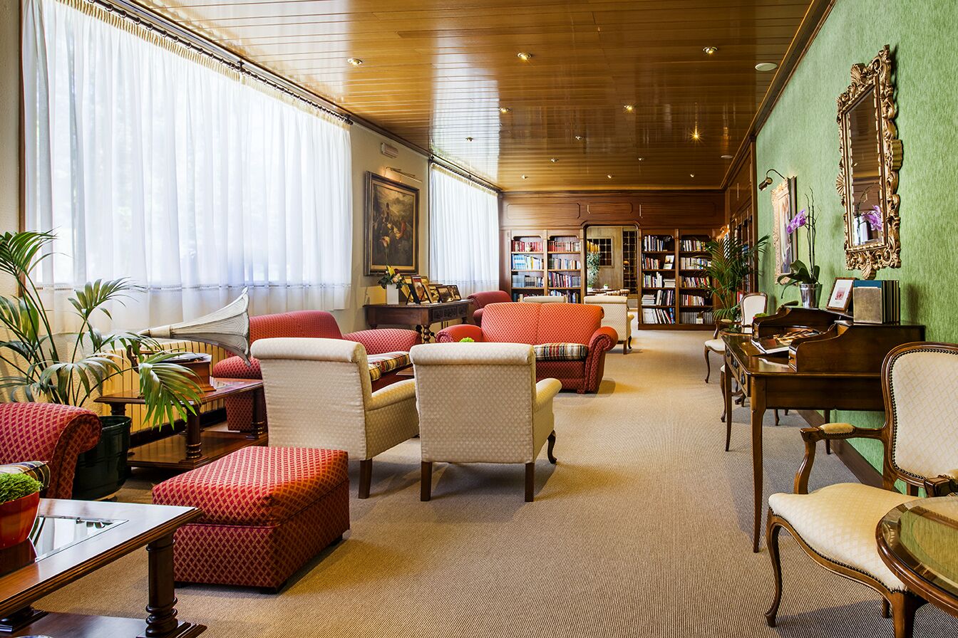 A spacious living room with multiple seating areas, a piano, and a bookshelf filled with books.