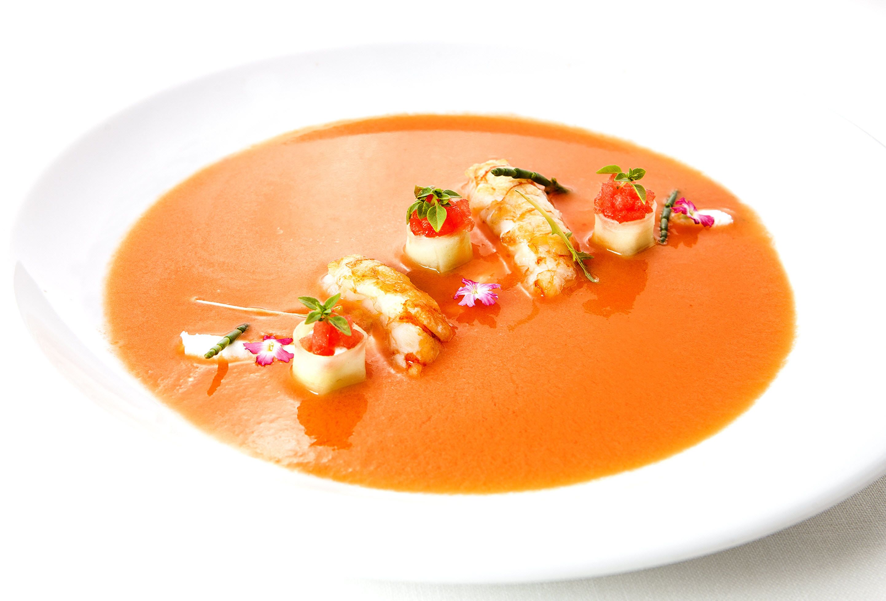Un plato blanco con sopa de tomate y adornos.
