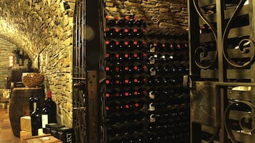 Une cave à vin avec un mur en pierre et des étagères métalliques où sont rangées les bouteilles de vin.