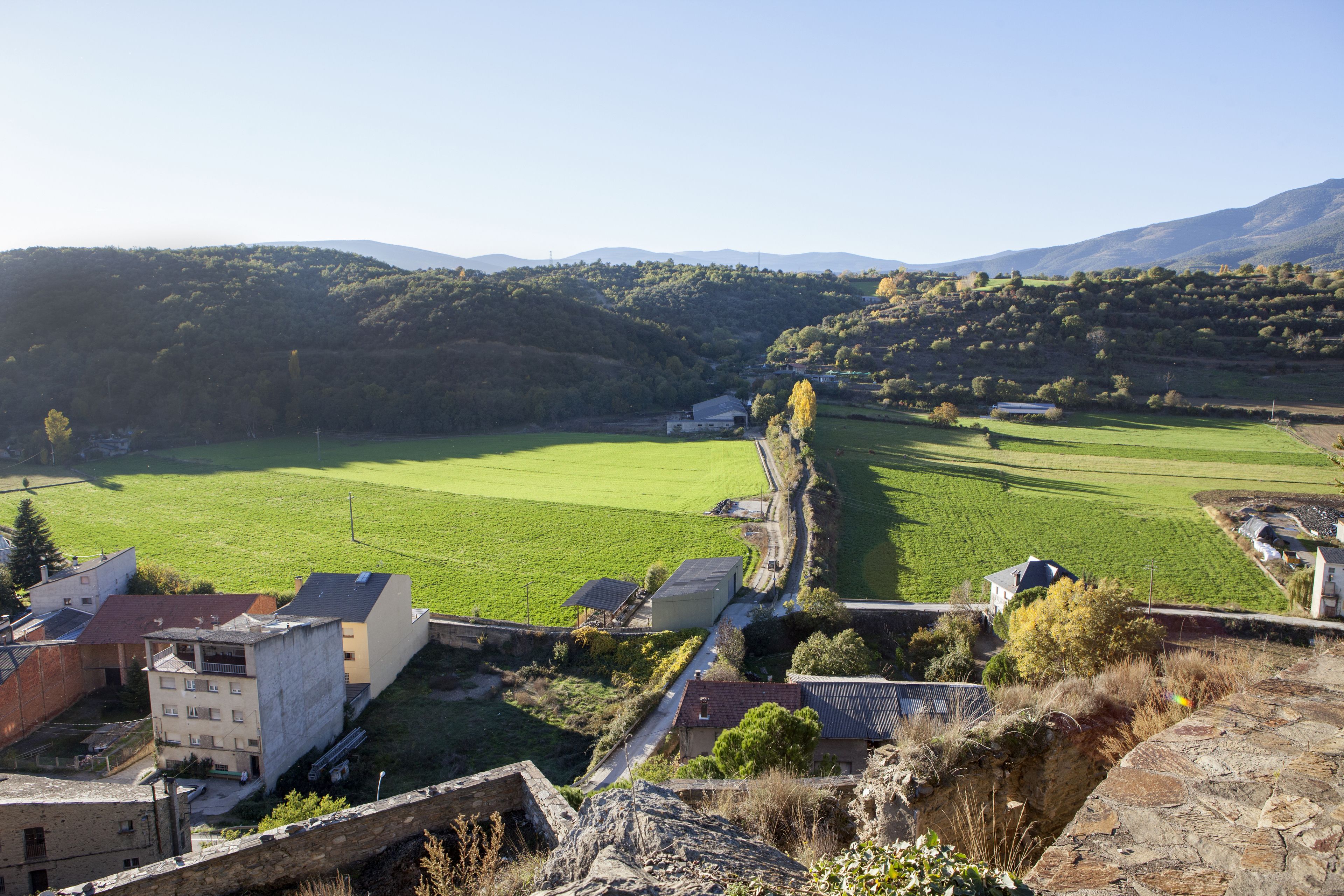 Ländliche Landschaft mit Steinmauer, Gebäuden und grünen Feldern.