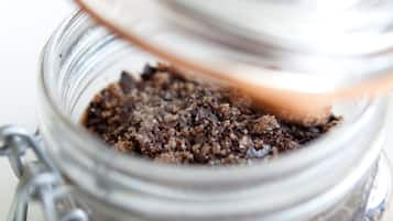 Un frasco de vidrio con tapa metálica, que contiene un material granuloso marrón.